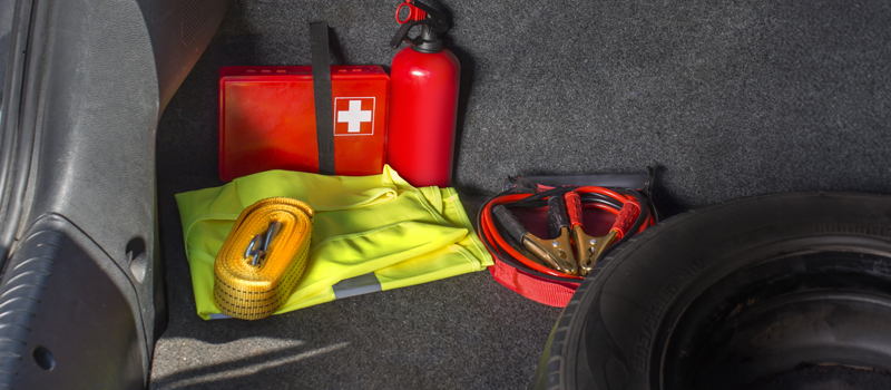 A picture of an emergency kit in a car, featuring a first-aid kit, a fire extinguisher, a tow strap, jumper cables, and a reflective vest.